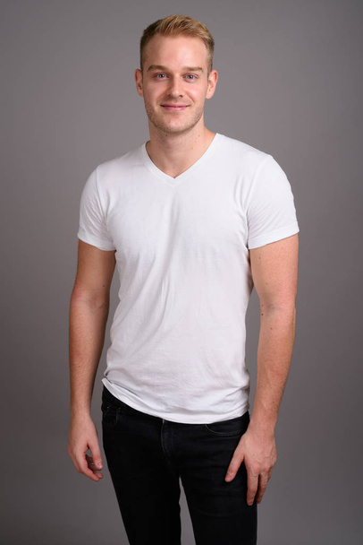 Junger schöner Mann mit blonden Haaren vor grauem Hintergrund - Foto, Bild