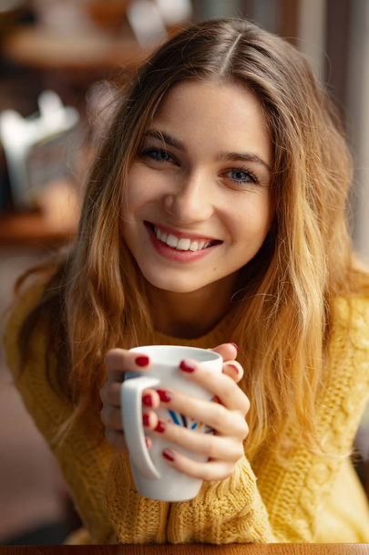 junge charmante Frau beim Kaffeetrinken, während sie in der Freizeit allein in einem Café sitzt. Porträt attraktive Frau mit einem süßen Lächeln, während sie sich im Café ausruhen. - Foto, Bild