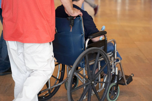 Baba oğluyla tekerlekli sandalye yuvarlanıyor. Yaşlı adam bir tekerlekli sandalye ve Yetişkin oğlu üzerinde yürüme. Bir adam babası taşıyor. Arkadan görünüm. - Fotoğraf, Görsel