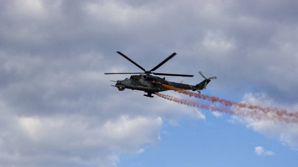 Helicóptero de combate con humo rojo en el cielo azul con nubes blancas. Vista desde la parte inferior
.  - Foto, Imagen
