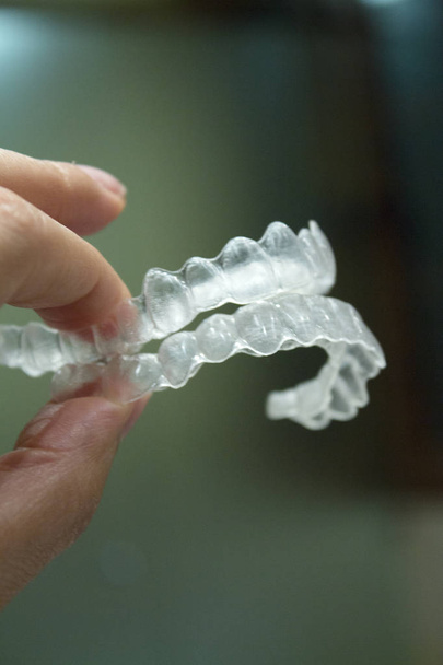 Womans ręki trzymającej przezroczyste stomatologicznej ortodoncji w celu poprawienia wyrównania stomatologiczne. Ciemne tło - Zdjęcie, obraz