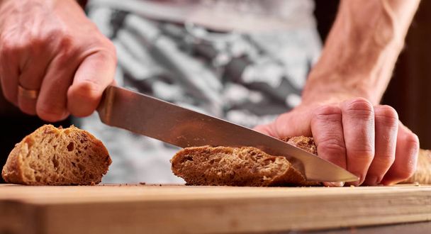 Whole grain bread put on kitchen wood plate with a chef holding gold knife for cut. Fresh bread on table close-up. Fresh bread on the kitchen table The healthy eating and traditional bakery concept - Foto, Imagen