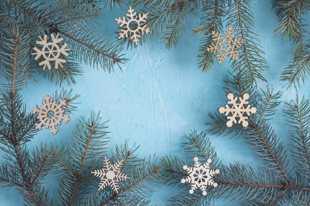 Karácsonyi keret felülnézet. Fenyő ágak és a fából készült hópelyhek a kék háttér - Fotó, kép