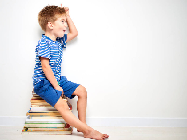 Маленький хлопчик сидить на стосі з книг
 - Фото, зображення