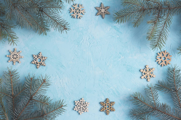 Christmas frame top view. Fir branches and wooden snowflakes on the blue background - Fotó, kép