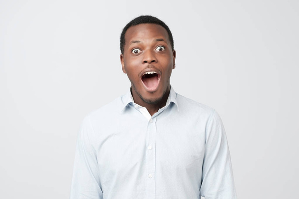 Headshot of surprised young dark-skinned man wearing casual blue shirt staring at camera with shocked look, expressing astonishment and surprise - 写真・画像