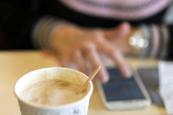 Giovane donna che utilizza uno smartphone mentre seduto in un caffè, beve delizioso caffè. sfocato
. - Foto, immagini