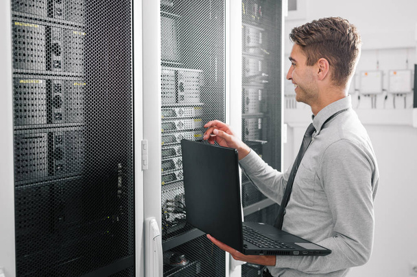 Male Server Engineer Works on a Laptop in Large Data Center. - Zdjęcie, obraz