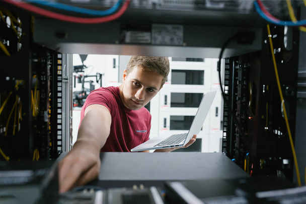  young man connecting wires in server cabinet while working with supercomputer in data center - Fotografie, Obrázek