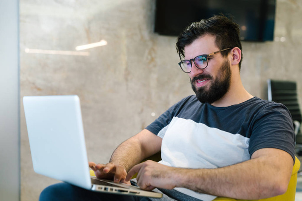Bearded man in  tshirt wearing eye glasses and using laptop at modern lightful office.Horizontal.Blurred background - Foto, afbeelding