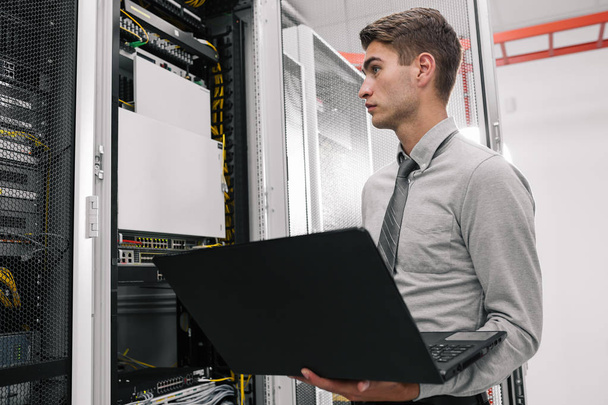  young man connecting wires in server cabinet while working with supercomputer in data center - Photo, Image