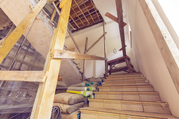 Construction materials, electrical wires, bags with cement, claircole  and putty, stairs with temporary wooden railing in  an apartment is during on the construction, remodeling, overhaul, rebuildi - Photo, image