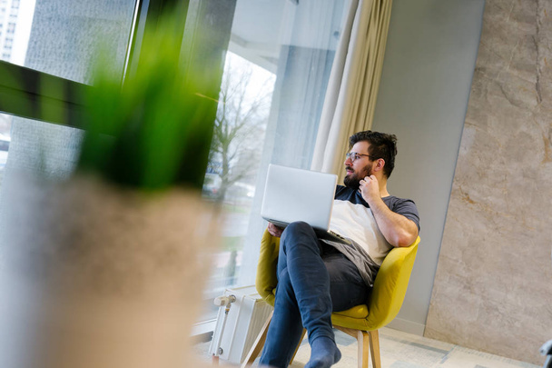 Bearded man in  tshirt wearing eye glasses and using laptop at modern lightful office.Horizontal.Blurred background - Photo, Image