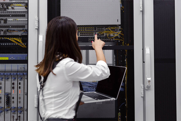 Técnica apecialista mujer utilizando el ordenador portátil al analizar el servidor en la sala de servidores
 - Foto, Imagen