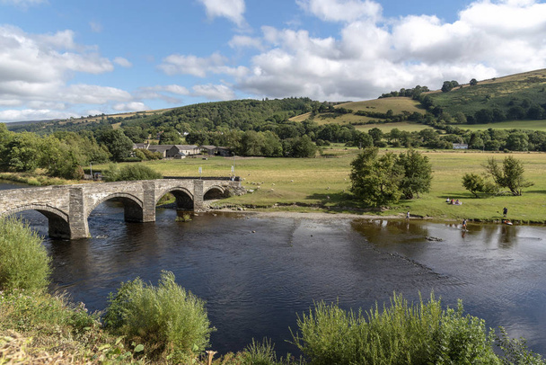 The River Dee en Carrog, Denbighshire, Gales del Norte, Ubicación panorámica en la orilla del río mirando hacia el viejo puente de piedra
 - Foto, Imagen