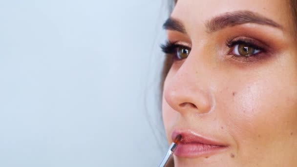 closeup young cute brunette woman putting lip gloss with makeup brush - Materiaali, video