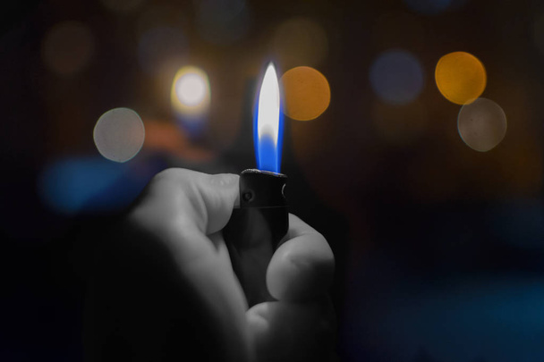Αναπτήρας με φωτιά στο χέρι στο φόντο της νύχτα τα φώτα στο bokeh. - Φωτογραφία, εικόνα