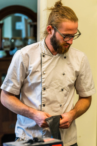 junger männlicher Koch denkt über die Zubereitung des Hochzeitsessens nach - weißes Hemd, verschwommener Hintergrund - Foto, Bild