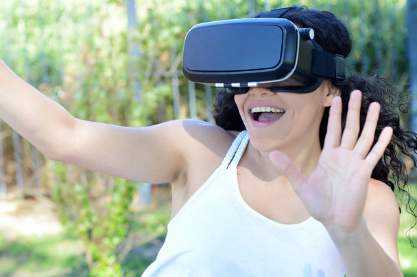 Young latin woman testing VR glasses outside in the park. VR headset glasses device.  - Foto, imagen