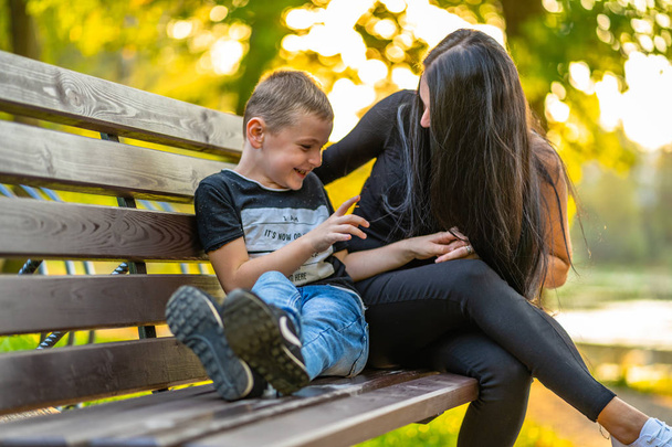 Mamma solletica suo figlio su un parco Benck in autunno con sfondo colorato in una giornata di sole, entrambi ridendo didascalia sulla camicia "Io sono, È ora o mai più, Mi chiedo, Perché sono qui
" - Foto, immagini