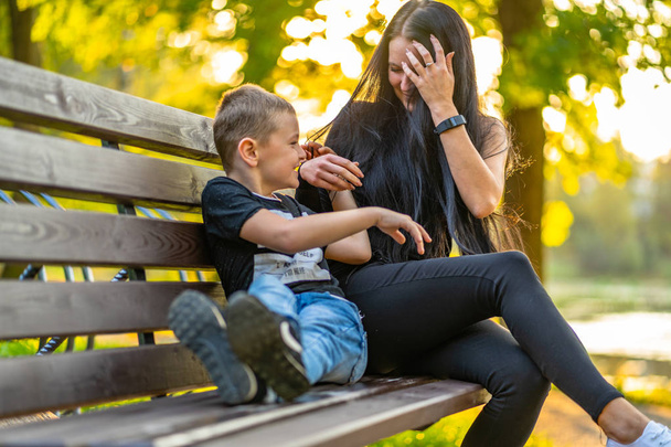 Mamma solletica suo figlio su un parco Benck in autunno con sfondo colorato in una giornata di sole, entrambi ridendo didascalia sulla camicia "Io sono, È ora o mai più, Mi chiedo, Perché sono qui
" - Foto, immagini
