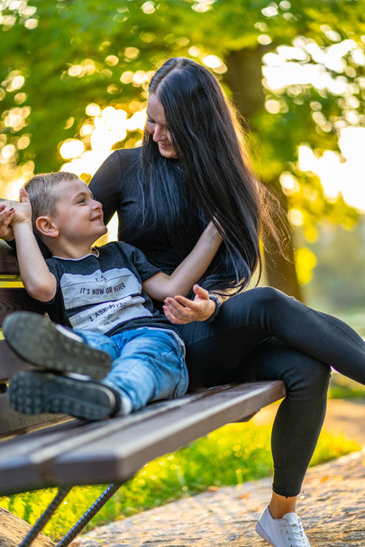 Mom Tickles Her Son on a Park Benck  in Autum with Colorful Backgroun in a Sunny Day, Both Laughing- Caption on Shirt "I am, It`s now or never, Iask myself, Why I`m here" - Photo, Image
