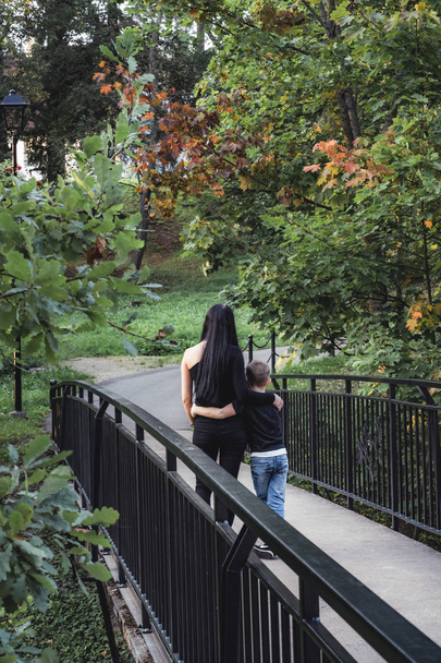 Kid Hugging His Mom and Walking Over the Bridge in a Park - Colourful Autumn Background - Foto, afbeelding