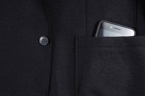 Black phone with camera in the pocket of blue jacket. - Photo, image