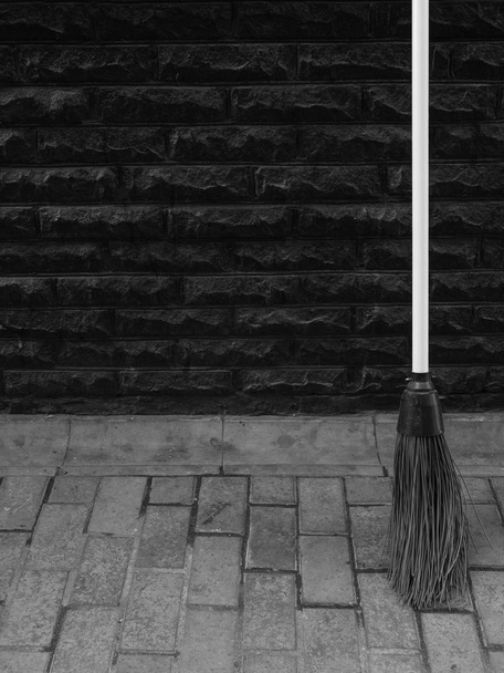 black and white photo of the broom at tile pavement near black wall. minimalistic cleaning business concept outdoor shot. improvement of public services - Valokuva, kuva