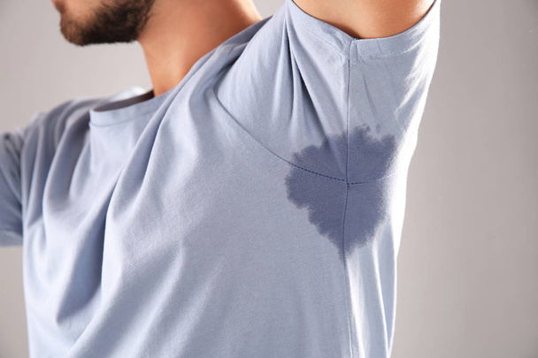 Sweaty man with stain on t-shirt against gray background, closeup. Using deodorant - Foto, Imagen