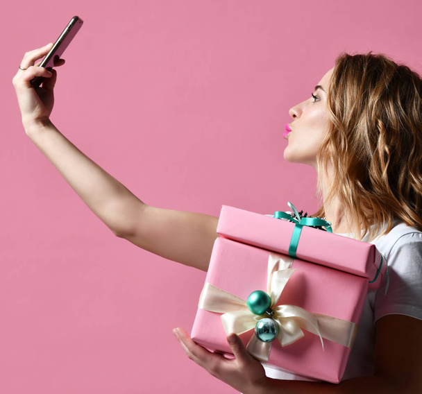 Молода красива жінка тримає різдвяні подарунки посміхаючись і робить селфі фото зі своїм мобільним телефоном
 - Фото, зображення