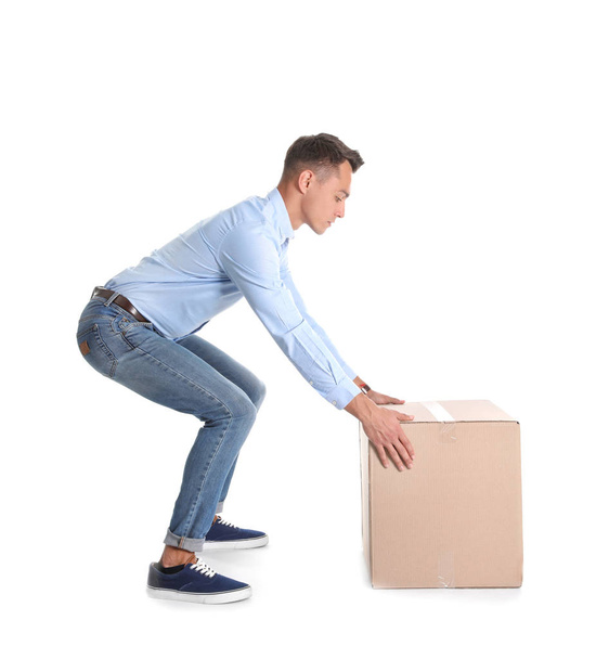Full length portrait of young man lifting heavy cardboard box on white background. Posture concept - Фото, зображення
