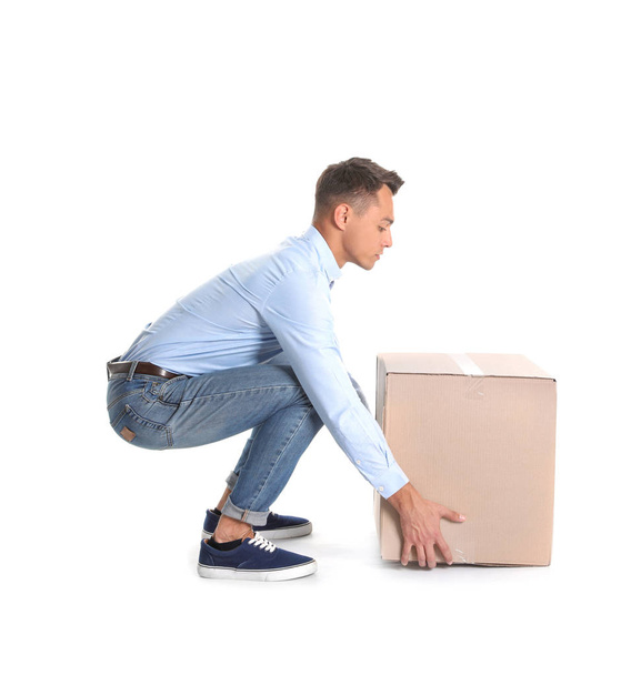 Full length portrait of young man lifting heavy cardboard box on white background. Posture concept - Photo, Image