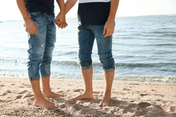 Gay couple standing barefoot on beach, closeup - Foto, afbeelding
