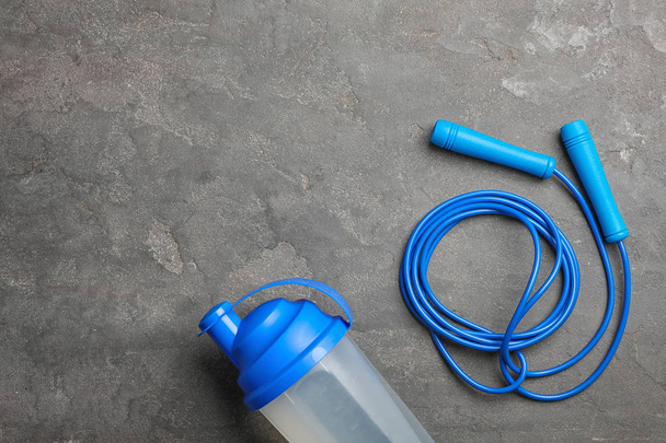Jump rope, bottle of water and space for text on grey background, top view - 写真・画像