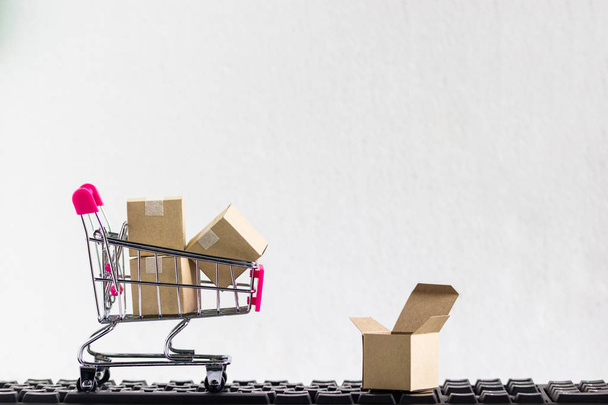 Online marktplaats, e-commerce concept: winkelwagentje met papier karton klaar om te winkelen op witte achtergrond en zwarte toetsenbord besteld door de klant via de media via internet Toon dat de handel. - Foto, afbeelding