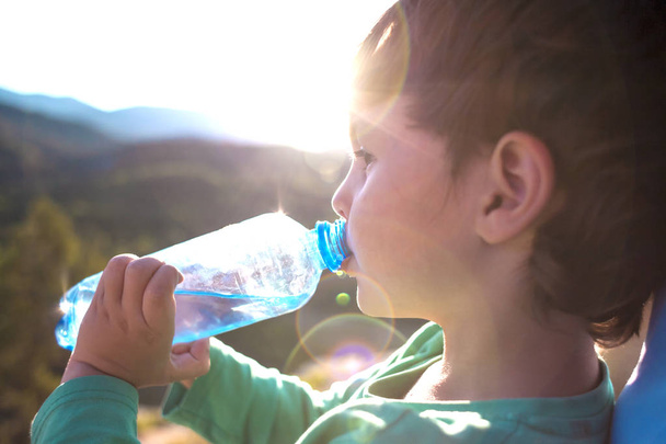 Ein Junge trinkt Wasser aus einer Flasche. löscht das Kind seinen Durst. das Kind reist durch die Berge. Müdes Kind ruht sich nach Spaziergang aus. - Foto, Bild