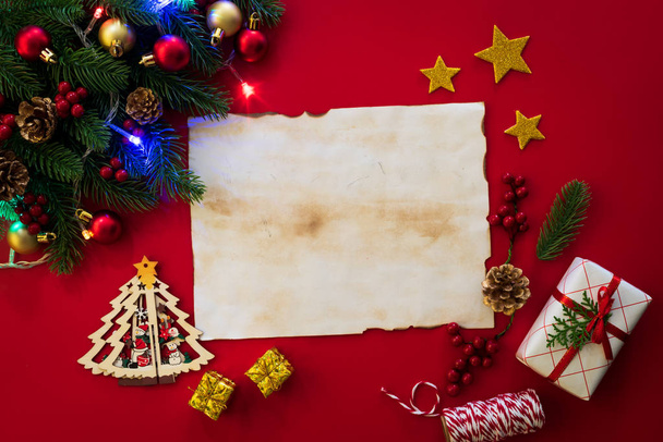 Vánoční pozadí konceptu. Pohled shora vánoční dárkové krabice starého papíru s smrkové větve, šišky, červené bobule a bell na červeném pozadí. - Fotografie, Obrázek