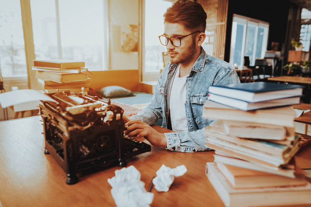 Text Writer Working on Typewriter Sits at Desk. Pensive Handsome Hardworking Freelance Screenwriter Scenarist Sits Near Stacks of Books Writing Play. Antique Retro Style of Work - Фото, изображение