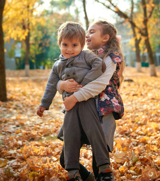 Dzieci bawią się na opadłych liści w parku miejskim jesień. - Zdjęcie, obraz