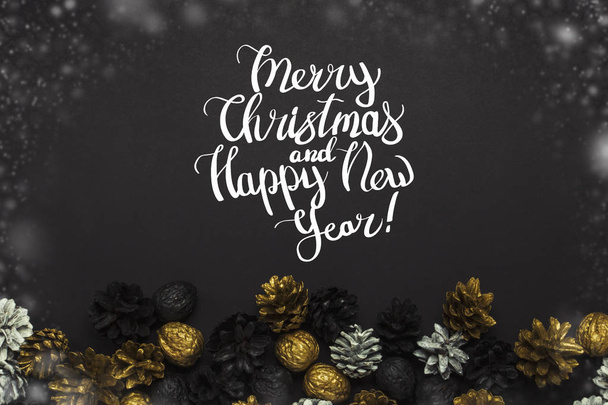 Cônes de pin et noix peints dans des couleurs dorées, noires, blanches sur un fond noir. Ajout du texte Bonne année et Joyeux Noël. Couché plat, vue du dessus
. - Photo, image