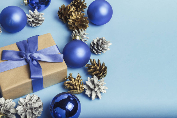 A kék szalag, karácsonyfadíszeket, labdák és a kék alapon fehér és arany fenyőtobozok díszdobozban. Kellemes karácsonyi ünnepeket és boldog új évet fogalmának. Minimalizmus. - Fotó, kép