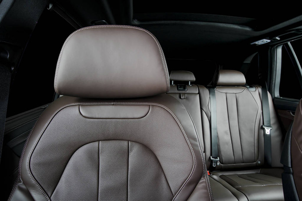 Moderní luxusní vůz hnědý perforovaný kožený interiér. Část kožených opěrek hlavy sedadel. Zadní sedadla v pozadí - Fotografie, Obrázek