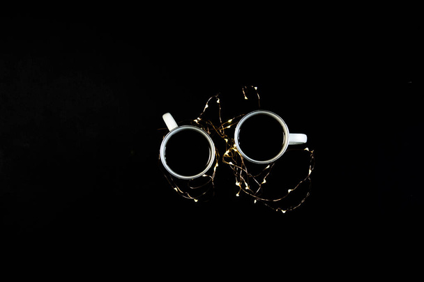 Two cups with coffee on black table with christmas lights. Photograph taken from above, top view with copy space. - Foto, imagen
