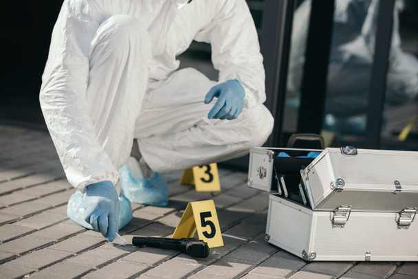 cropped view of male criminologist in protective suit and latex gloves sitting near evidence gun - Photo, Image