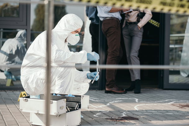 criminólogo masculino en traje de protección y guantes de látex recogiendo pruebas en la escena del crimen
 - Foto, Imagen