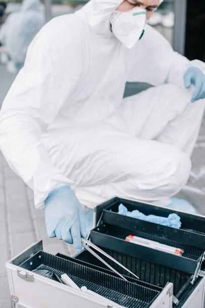 criminólogo masculino en traje de protección y guantes de látex tomando pinzas de bolsa de herramientas de investigación
  - Foto, Imagen
