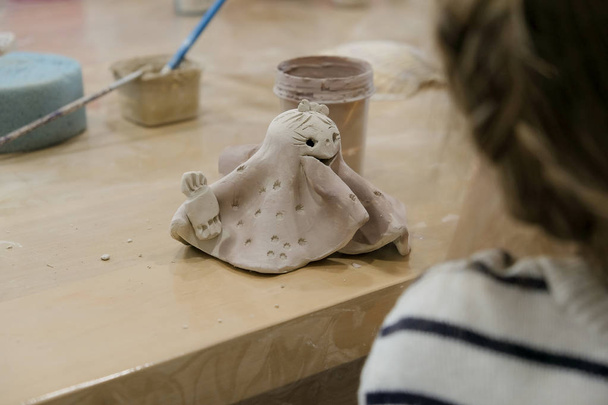 Een kind schildert zijn kleibeeldje in een atelier tijdens een modellenles. - Foto, afbeelding