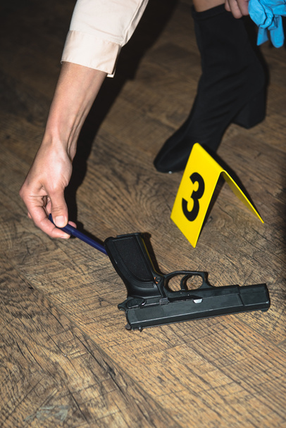 visão recortada da mão examinando arma perto de marcador de evidência na cena do crime
 - Foto, Imagem