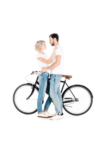 Attractive couple hugging while standing near the bicycle isolated on white - Zdjęcie, obraz